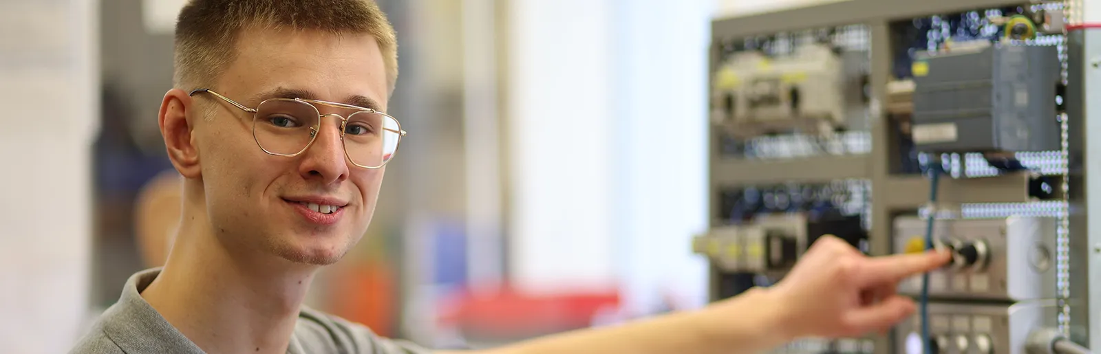 Elektroniker-lts Junger Mann blickt in die Kamera, während er einen Hebel an einer Schaltanlage bedient.