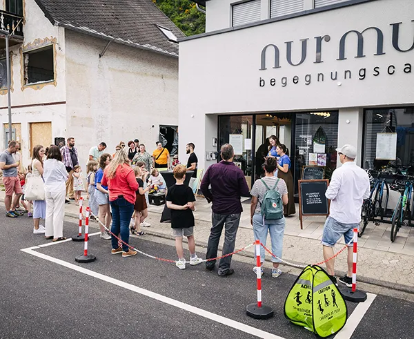 Menschen auf einer Straße vor zwei Häusern mit externem Link zum Hoffnungswerk e.V.