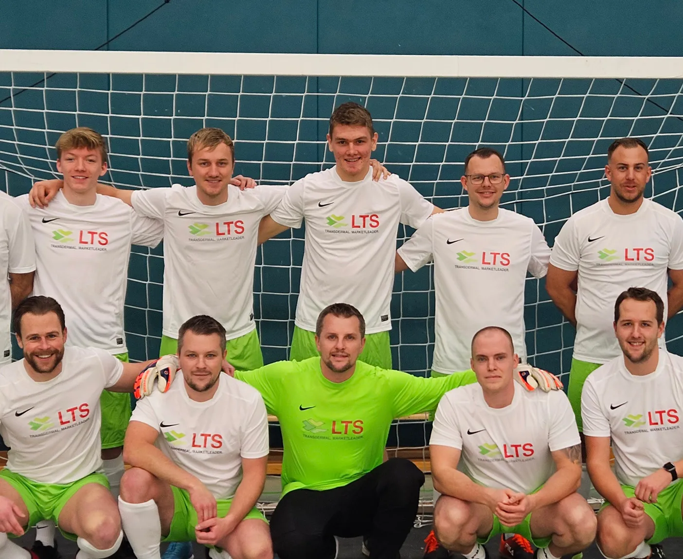 Die LTS-Fußballmannschaft in weißen Trikots mit LTS-Logo und grünen Shorts vor einem Tor; über dem Bild liegt der Text ‚LTS Betriebsfußball‘.