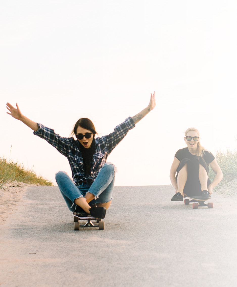 Zwei Frauen sitzen auf Skateboards und fahren eine Straße hinab: LTS gibt sein Wissen transparent und ehrlich weiter.