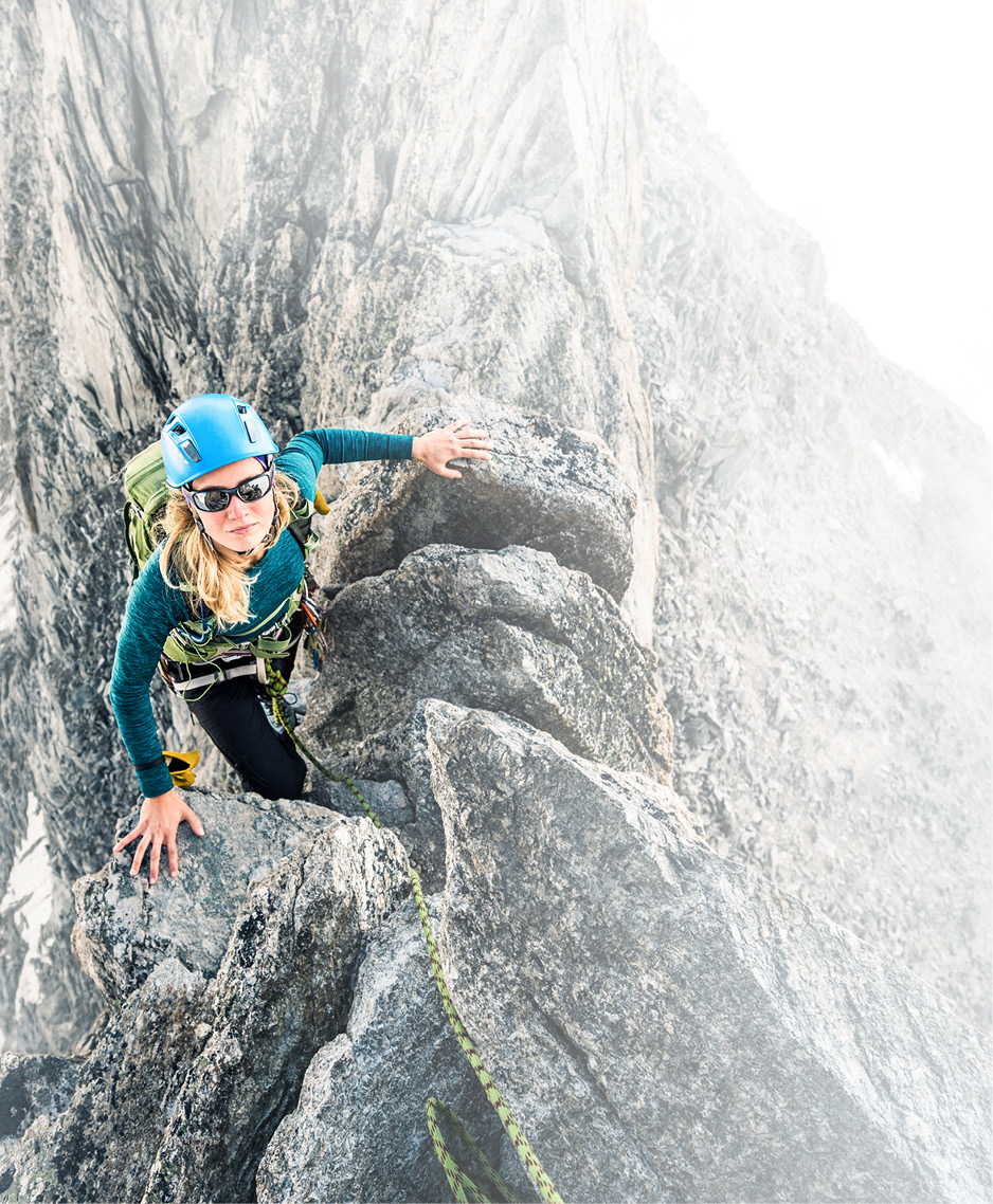 Eine Frau mit Kletterausrüstung schaut von einem steilen Felsgipfel hoch: LTS fördert die Stärken jedes Einzelnen.