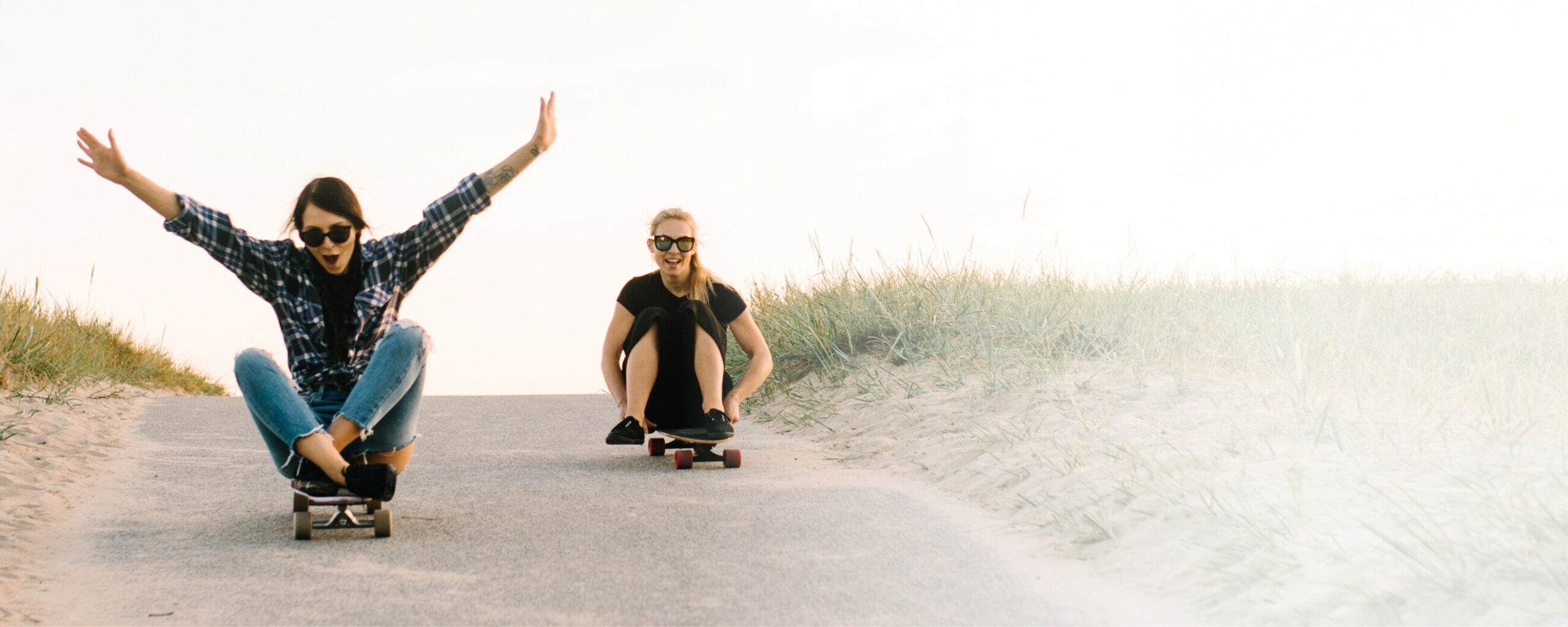 Zwei Frauen sitzen auf Skateboards und fahren eine Straße hinab: LTS gibt sein Wissen transparent und ehrlich weiter.