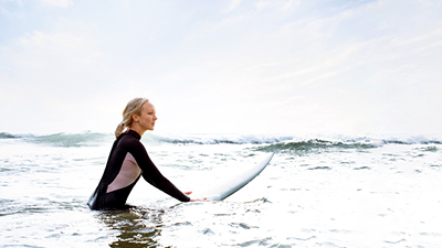 Frau im Surfanzug und Surfboard im Wasser: Bildnachweise des LTS-Jobportals
