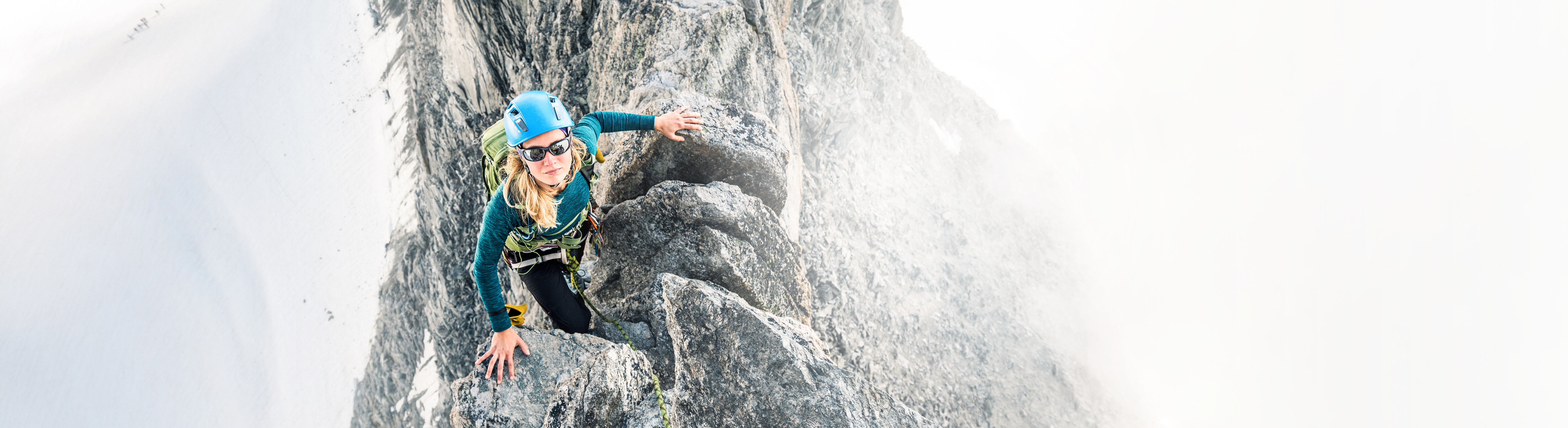 Eine Frau mit Kletterausrüstung schaut von einem steilen Felsgipfel hoch: LTS fördert die Stärken jedes Einzelnen.