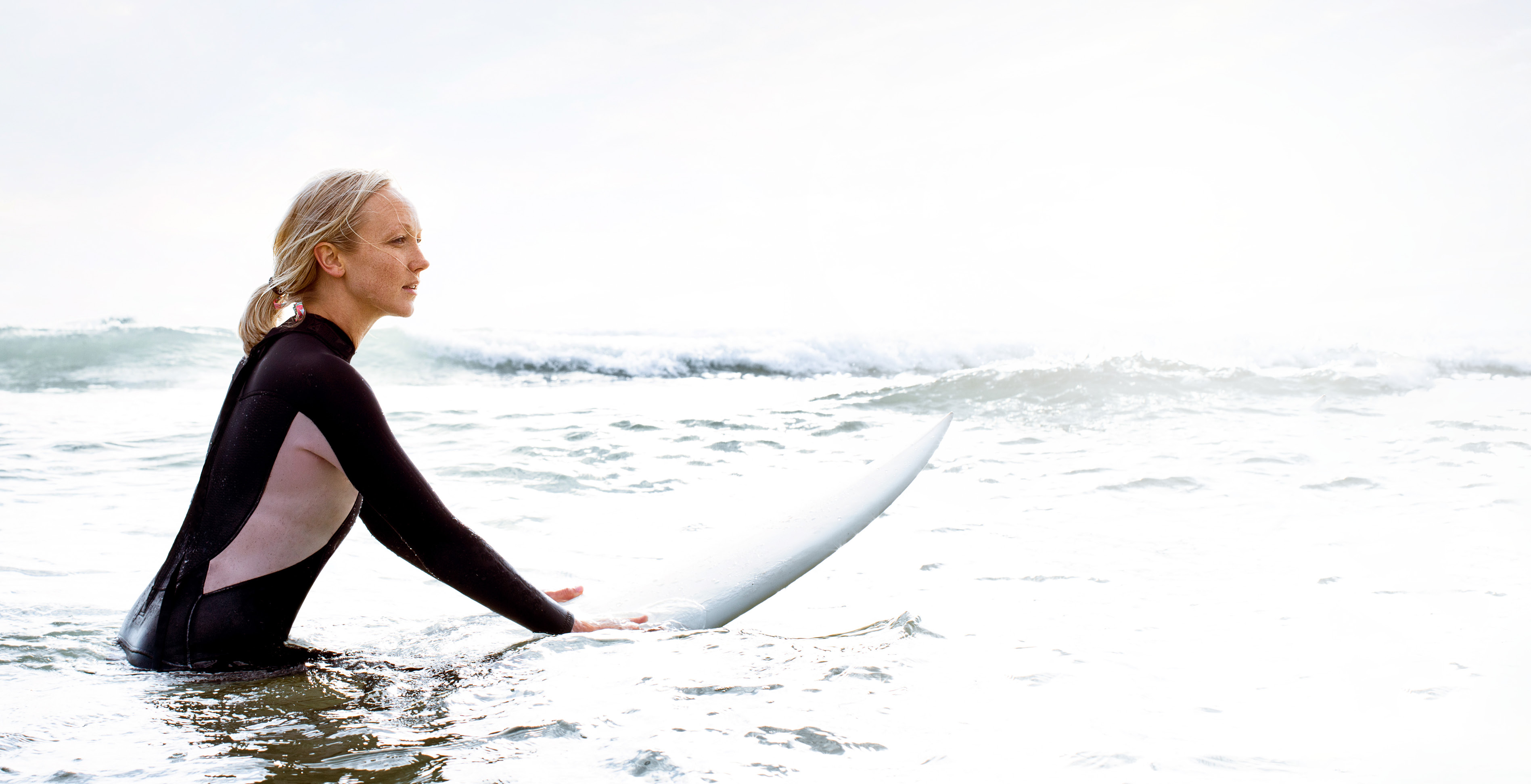 Frau im Surfanzug und Surfboard im Wasser: Erlebe den Flow: Dein Weg. Deine Zukunft. Dein LTS.