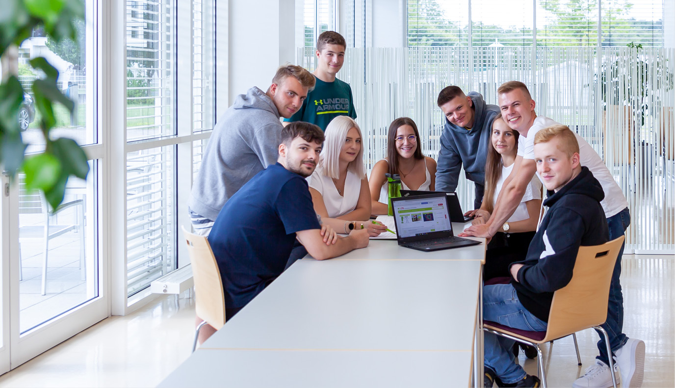 Eine Gruppe von LTS-Lehrlingen steht und sitzt um einen Tisch: Es gibt zahllose Gründe für eine Ausbildung bei LTS.