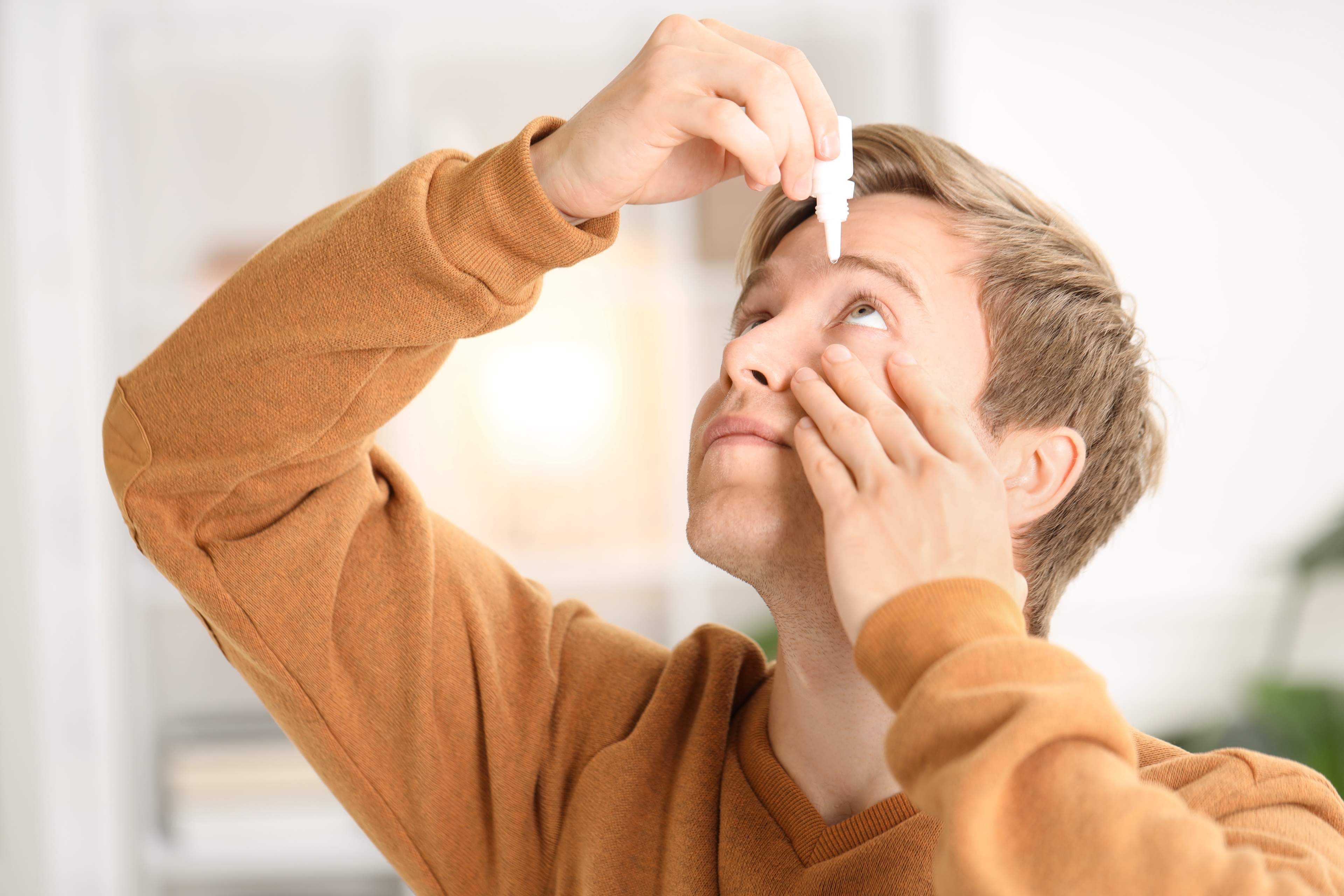Young,Man,Applying,Eye,Drops,At,Home